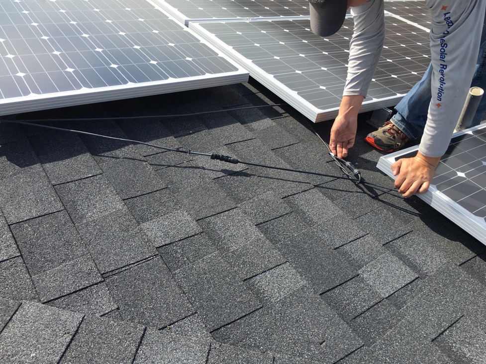 Technician working on wiring beneath residential solar panels during solar system maintenance or repair.